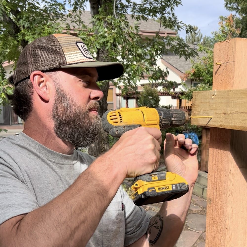 Drew driving a screw into a fence post with a cordless drill
